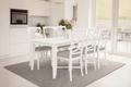 A white Hampton acacia timber dining table set with six chairs, round silver metal handles, and light grey upholstery, displayed in a bright dining room setting.