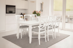 A white Hampton acacia timber dining table set with six chairs, round silver metal handles, and light grey upholstery, displayed in a bright dining room setting.
